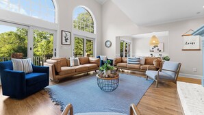 A spacious living room with high ceilings, large windows, and a view of greenery outside. - Waterfront, Pool & Dock | Shoreway Cove by AvantStay (Huntersville)