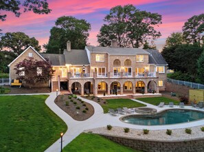 A large, multi-story house with a swimming pool, multiple balconies, and a well-maintained lawn.