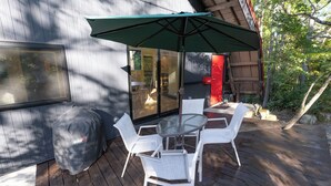 An outdoor patio with a table and chairs, a green umbrella, and a glass door leading to an interior space. - KONAYUKI CABIN HAKUBA (Hakuba)