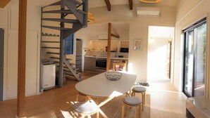 A modern kitchen with a spiral staircase, a dining area with a white table and stools, and a large window providing natural light. - KONAYUKI CABIN HAKUBA (Hakuba)