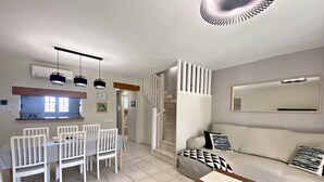 Uma sala de estar moderna com sofá, mesa de jantar com cadeiras, escada e um espelho grande na parede.