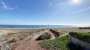 Uma praia com céu claro, um caminho de areia e uma cerca que leva à água.
