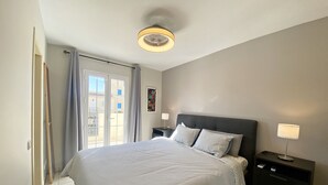 Quarto com uma cama grande, duas mesas de cabeceira com luminárias, uma luz no teto e vista para o exterior por uma porta de correr.