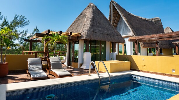 A poolside area with lounge chairs, a thatched-roof structure, and a clear blue sky.