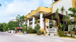 A hotel with a yellow facade, palm trees, and a sign reading "Pueblo Escondido".