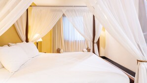 A bed with white linens, a canopy, and a bedside table with a lamp.