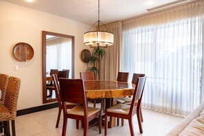 A dining area with a wooden table and chairs, a hanging light fixture, and a large mirror on the wall.