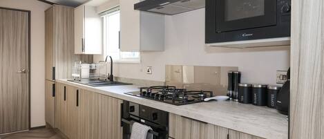 A modern kitchen with wooden cabinets, a gas stove, a microwave, and a window providing natural light.