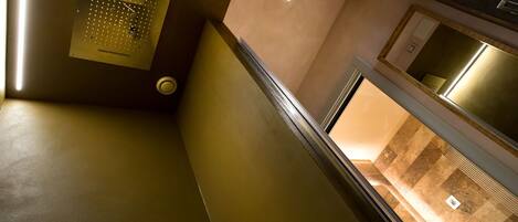 A modern interior with a metallic panel, a recessed ceiling light, and a view of a bathroom with a sink and mirror.