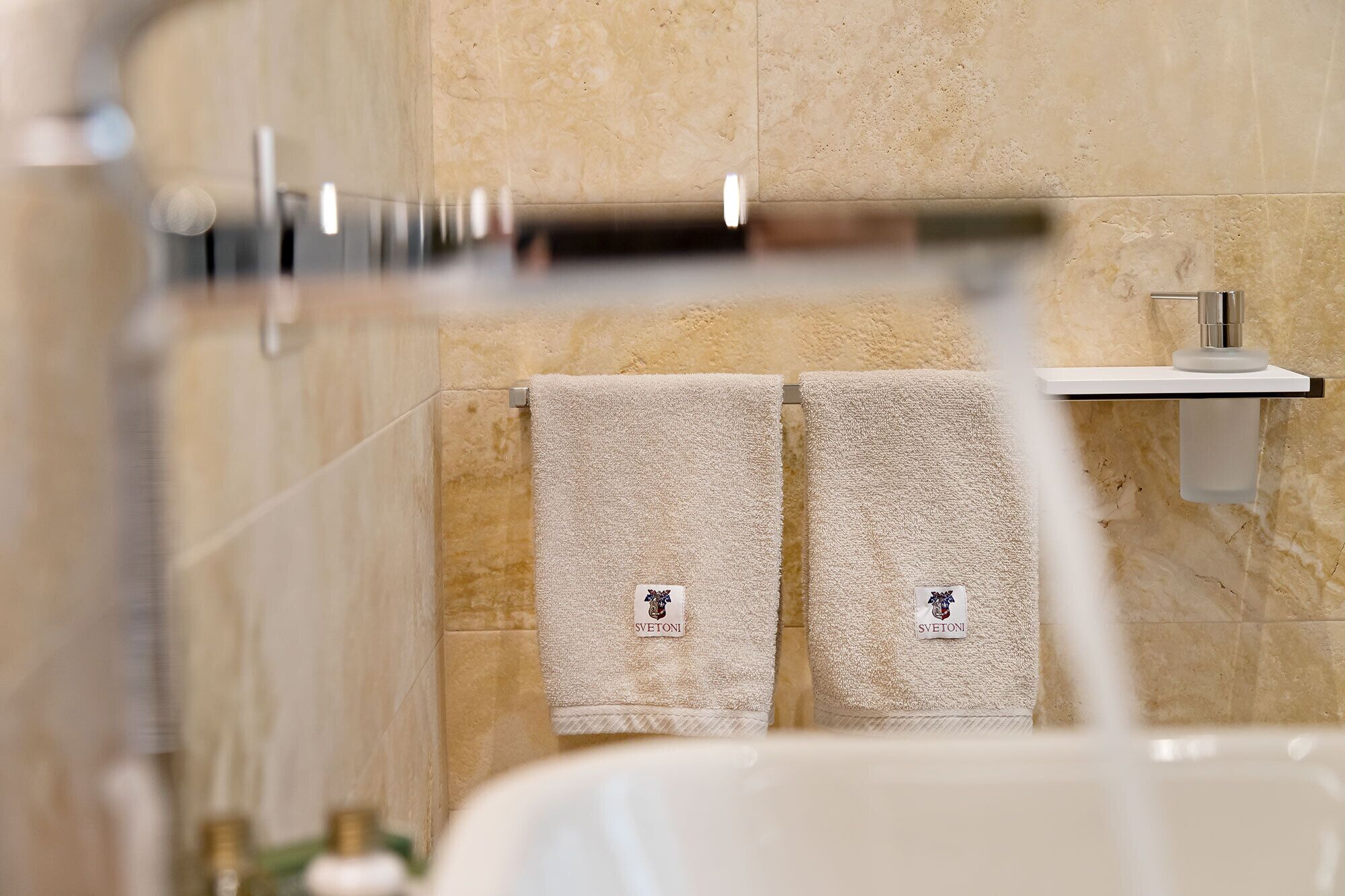 A bathroom with beige tiles, a white sink, and two towels hanging on a rack.