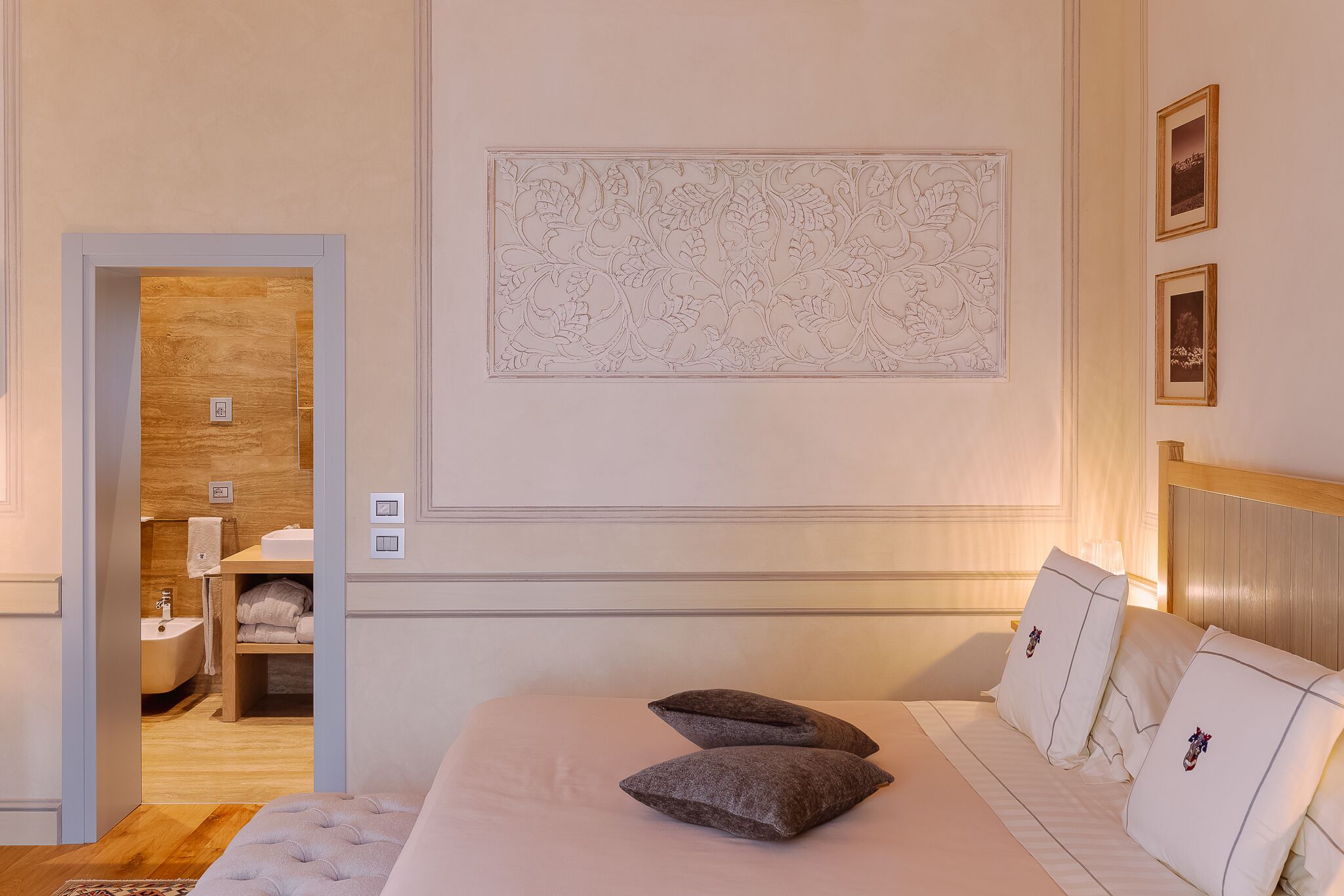 A hotel room with a bed, two pillows, a nightstand, a wall-mounted artwork, and a bathroom visible through an open door.