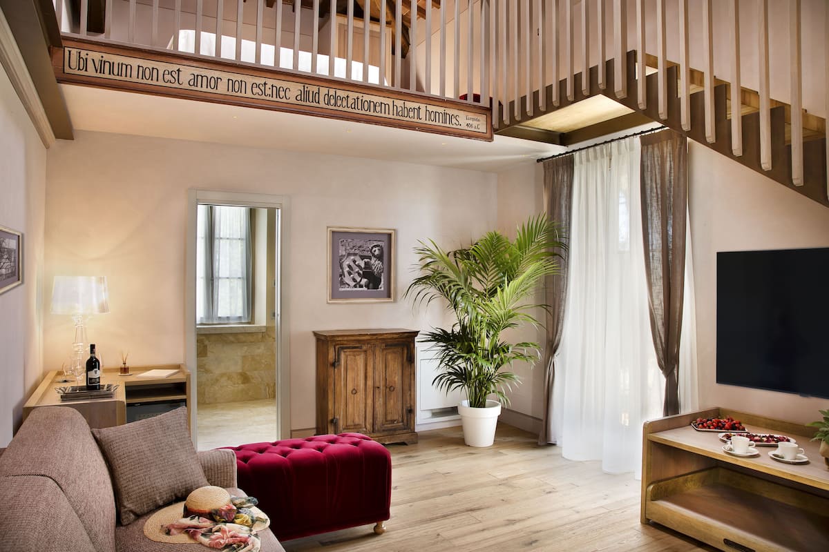 A living room with a red ottoman, a wooden cabinet, a potted plant, a flat-screen TV, and a staircase with a wooden railing.