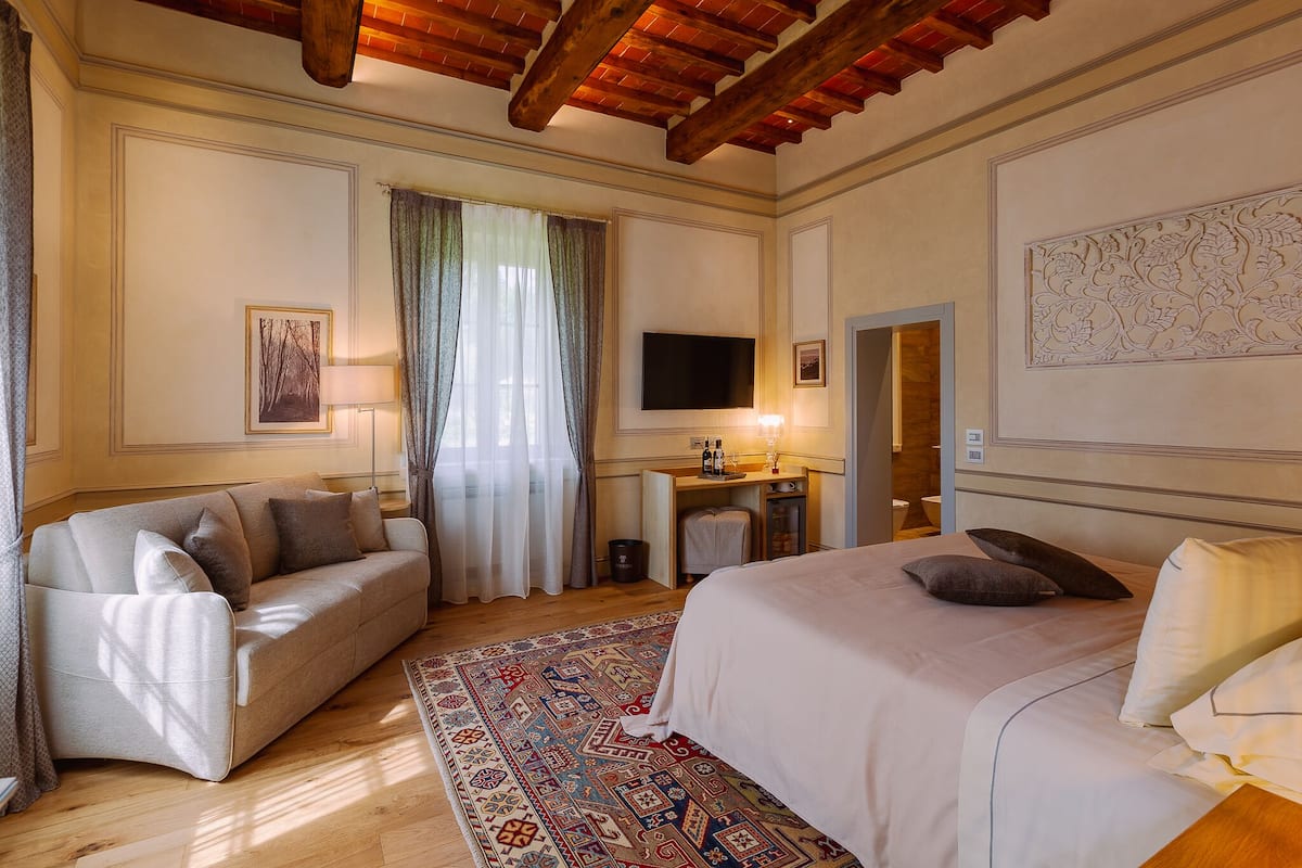 A hotel room with a bed, a sofa, a TV, a desk, and a patterned rug.