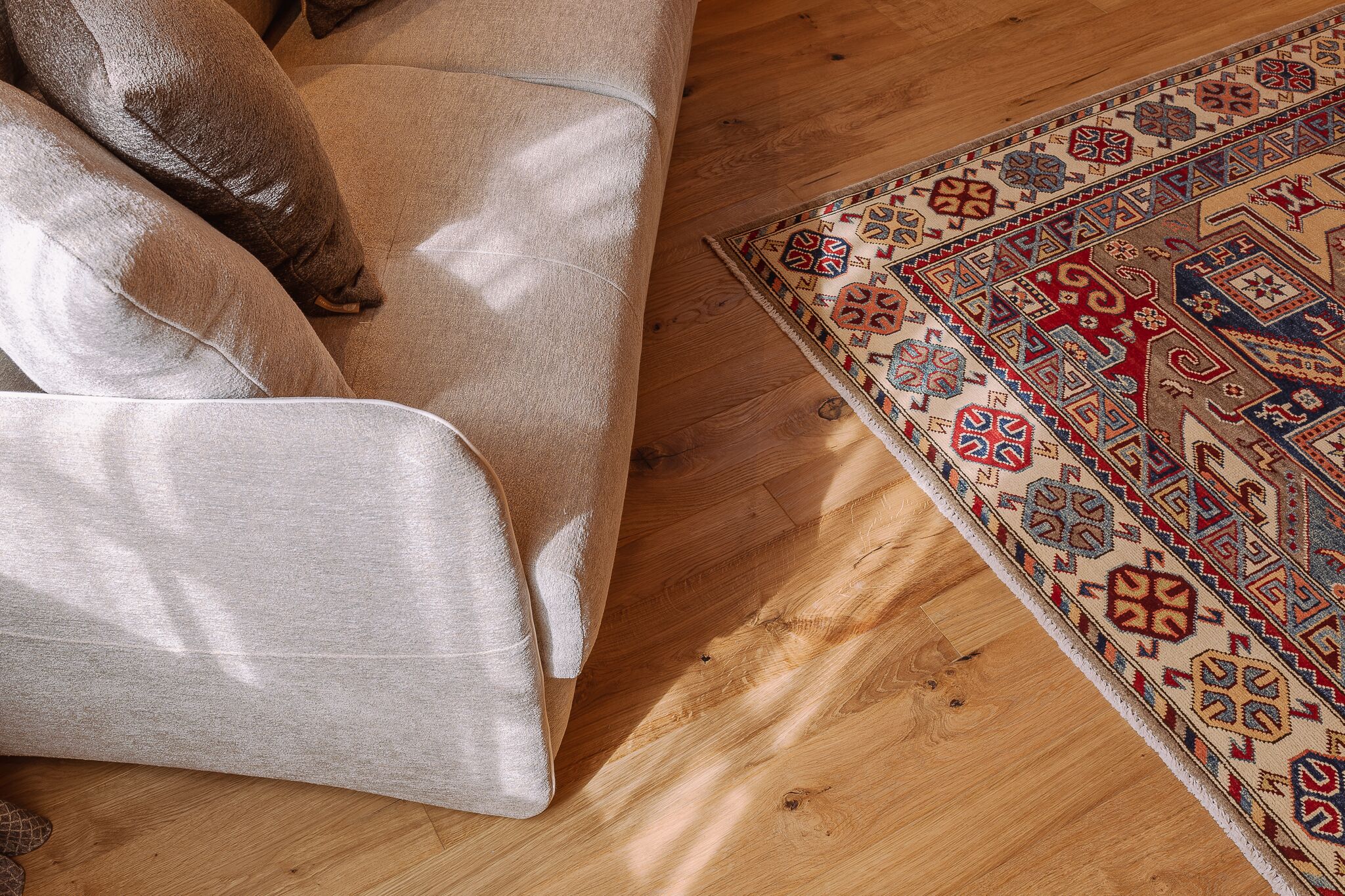 Ein beiges Sofa mit einem gemusterten Teppich auf Holzboden.