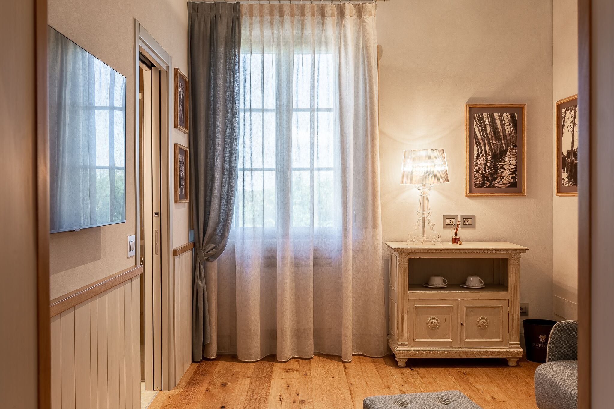 A room with a wooden floor, a white cabinet with two shelves, a lamp, and a framed picture on the wall.