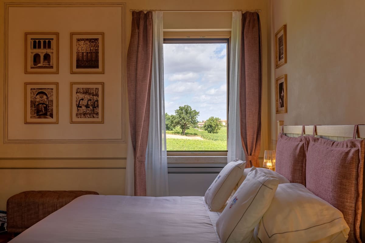 A hotel room with a bed, a window with curtains, and four framed pictures on the wall.