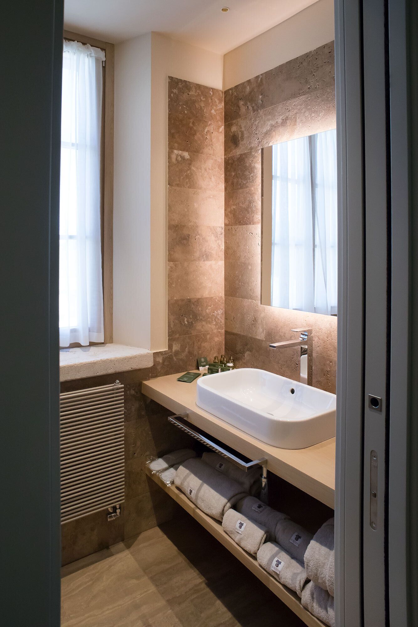 Une salle de bain moderne avec une grande baignoire, un meuble-lavabo et un miroir au-dessus du lavabo. Il y a une fenêtre avec des rideaux et un porte-serviettes avec des serviettes.