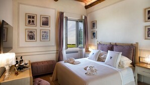 Habitación de hotel con una cama grande, una mesita de noche con lámpara, un banco y cuadros enmarcados en la pared.