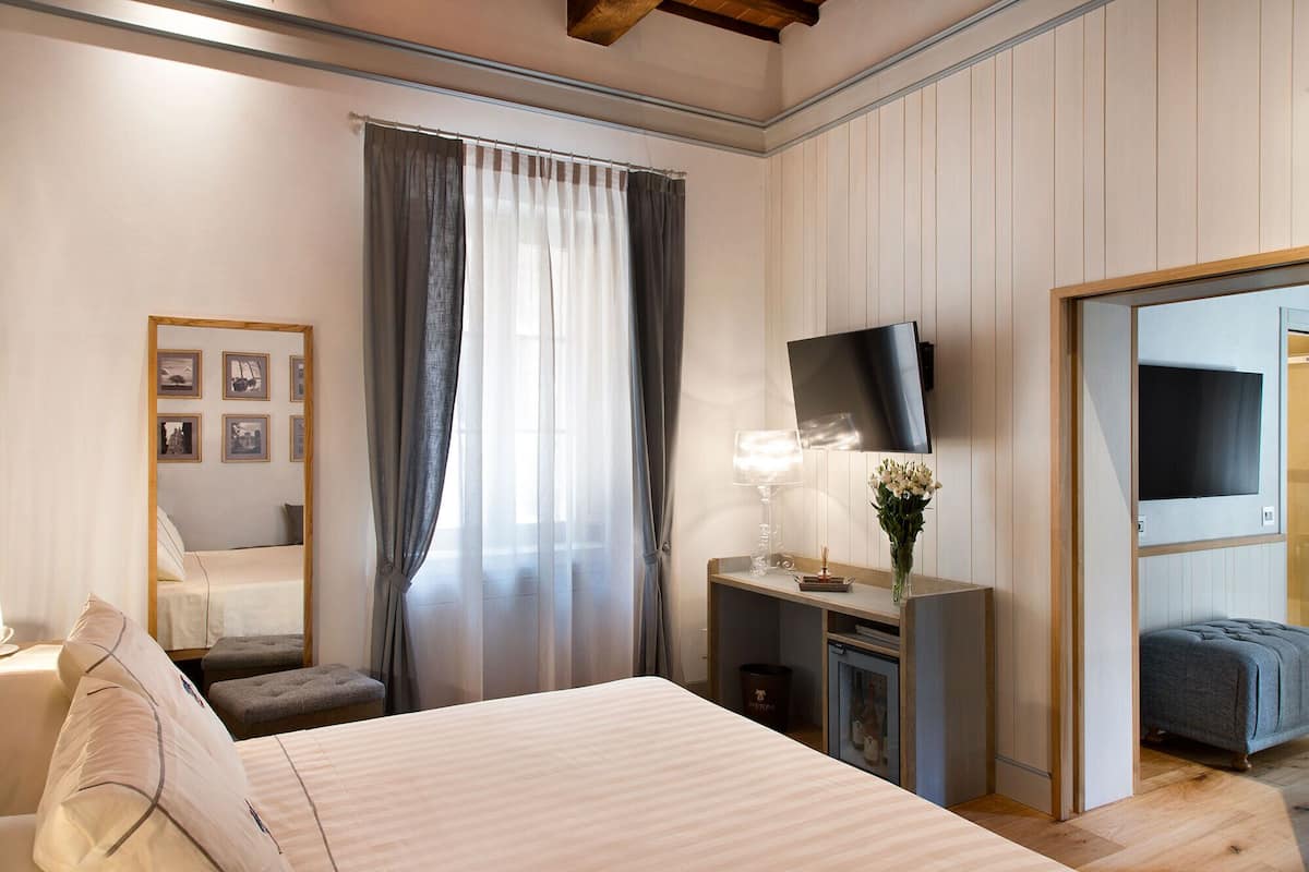 A bedroom with a large bed, a bedside table with a lamp, a TV mounted on the wall, and a small seating area.