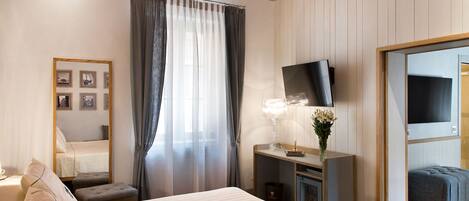 Un dormitorio con una cama grande, una mesita de noche con lámpara, un televisor montado en la pared y un pequeño rincón de descanso.