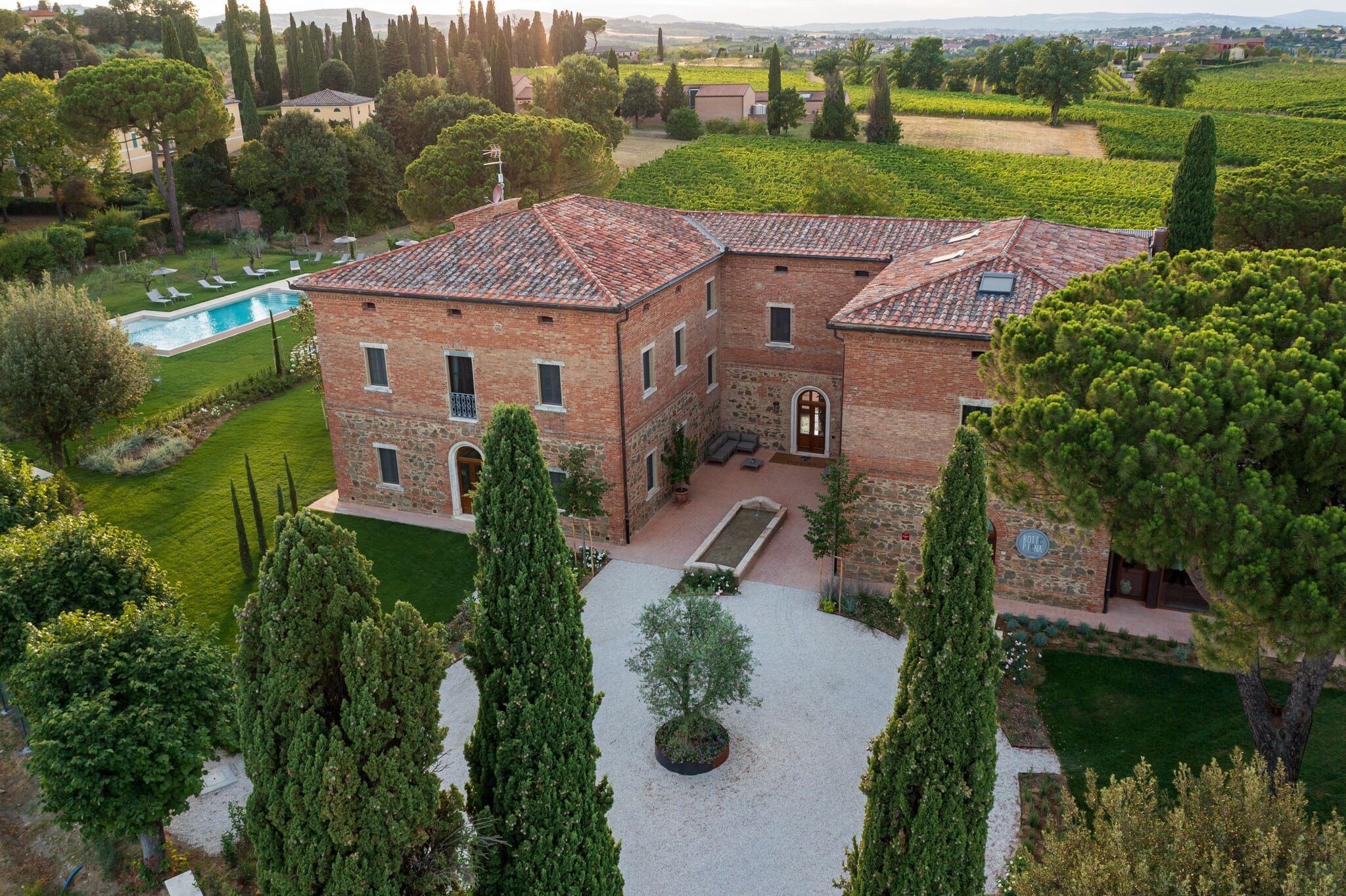 A large brick building with a courtyard, surrounded by trees and a swimming pool.