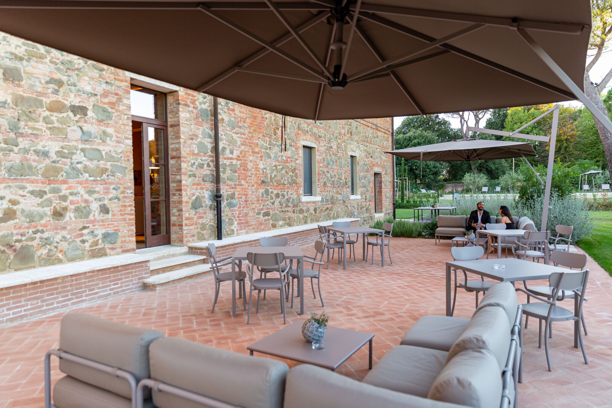 Un espace extérieur aménagé en terrasse, avec des murs en pierre, des tables, des chaises et un coin salon abrité.