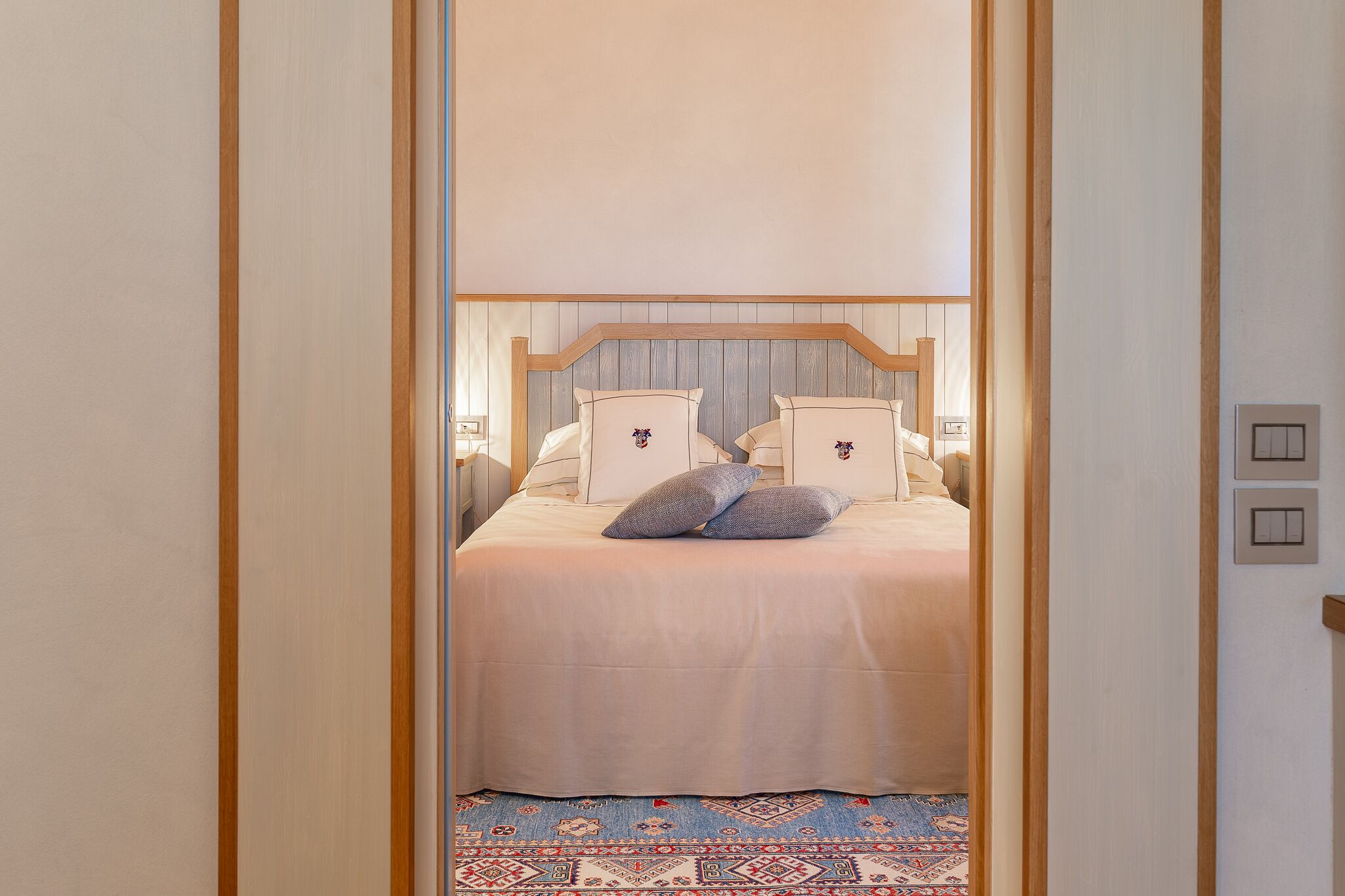 A bedroom with a bed, pillows, and a patterned rug.