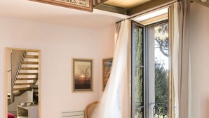 Una habitación con un ventanal grande, una silla, una mesita y un espejo.