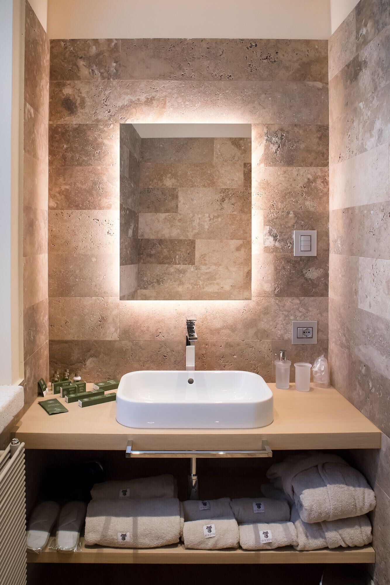 Un baño con un espejo rectangular grande, un lavamanos blanco y un perchero con toallas dobladas.