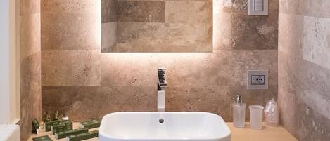 Un baño con un espejo rectangular grande, un lavamanos blanco y un perchero con toallas dobladas.