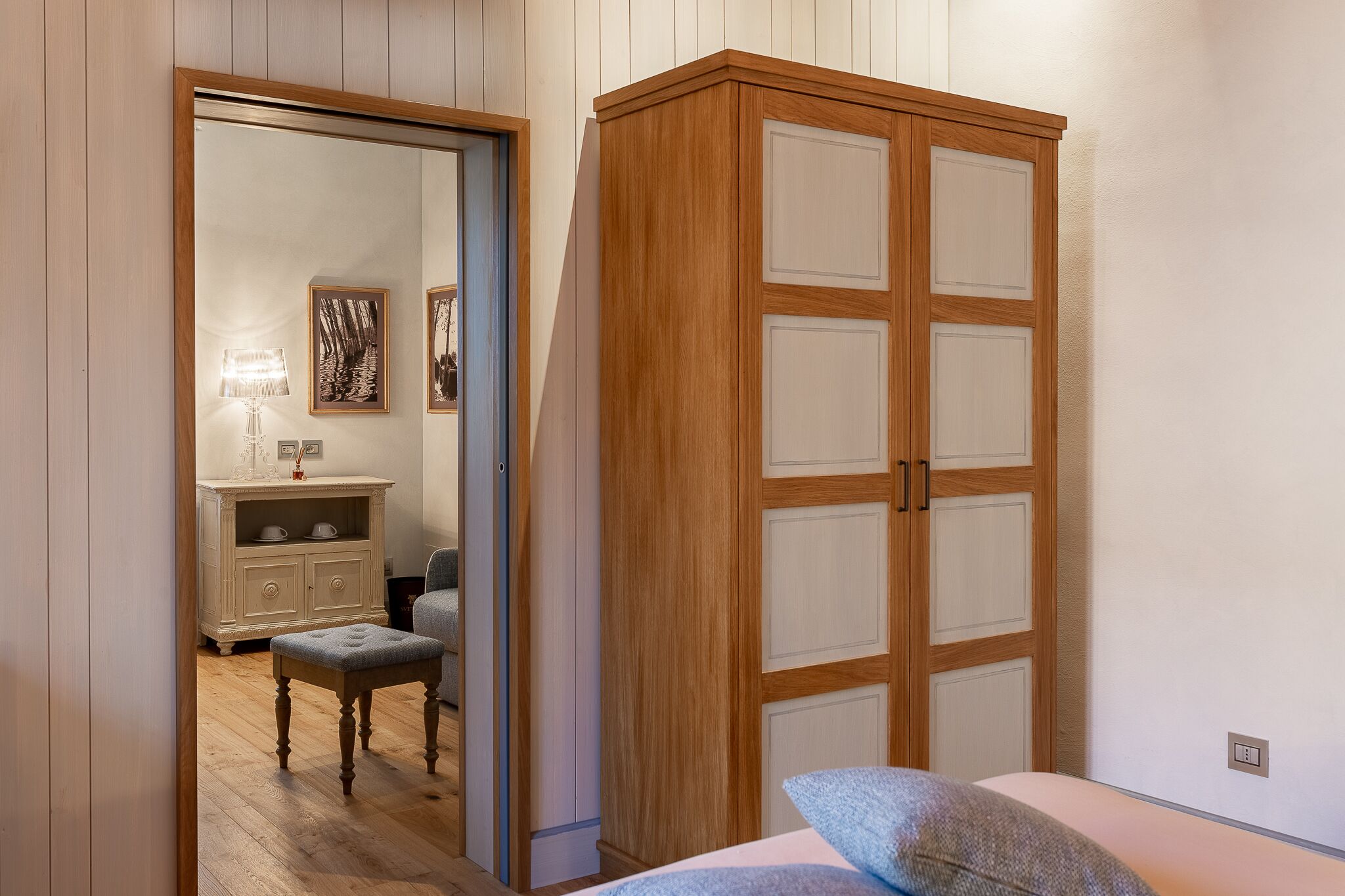 A bedroom with a wooden wardrobe, a bedside table, and a chair.