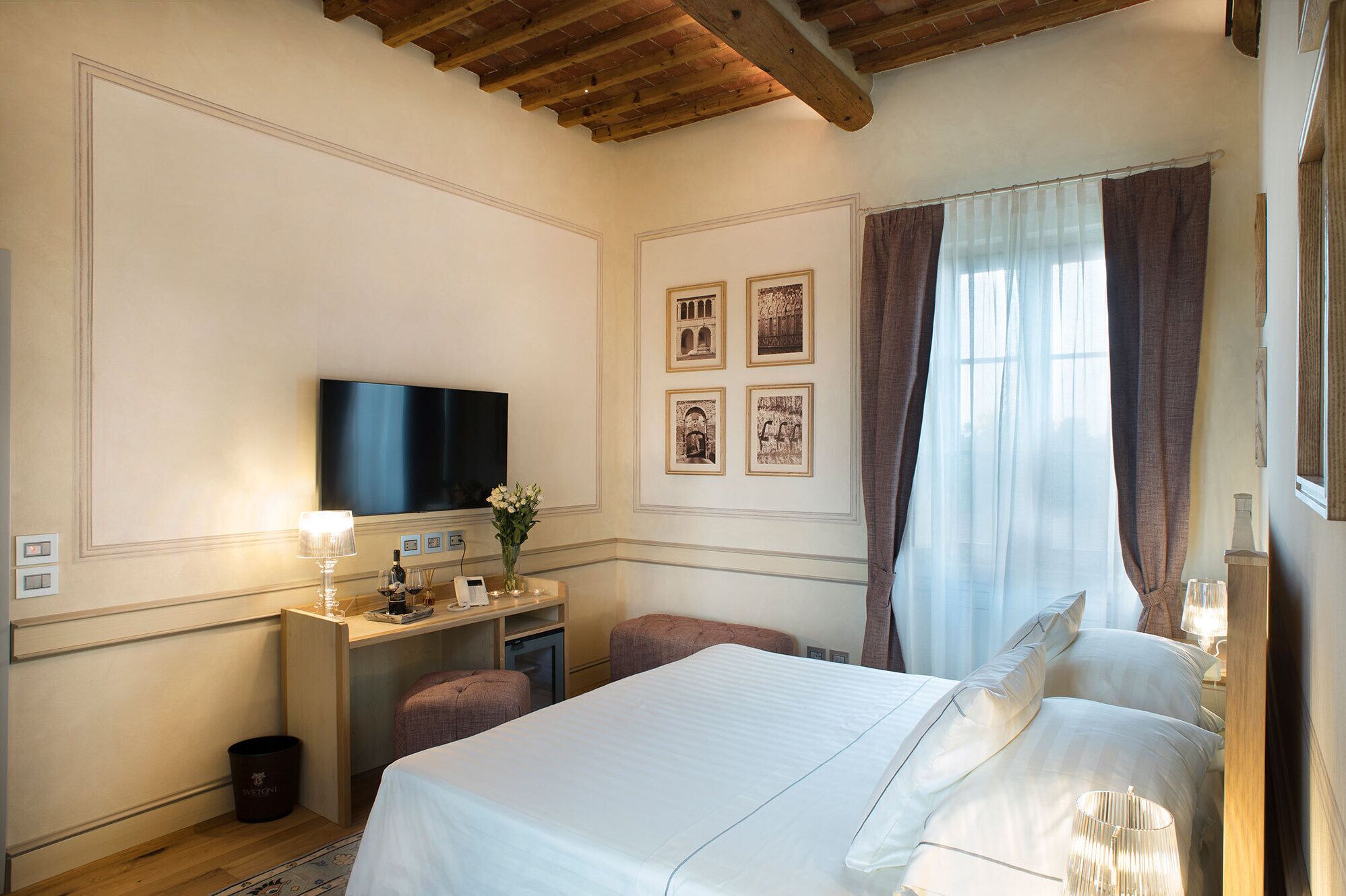 Ein Hotelzimmer mit einem Bett, einem Schreibtisch mit Fernseher, einem kleinen Tisch mit Lampe und einer Wand mit gerahmten Bildern.
