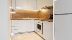 Una cocina moderna con armarios blancos, horno empotrado y refrigerador de acero inoxidable.