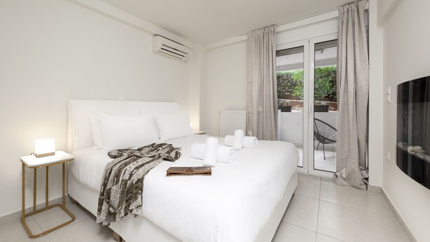 Habitación de hotel moderna con una cama grande, una mesita de noche con lámpara, vistas al exterior a través de un ventanal corredero y un televisor de pantalla plana en la pared.