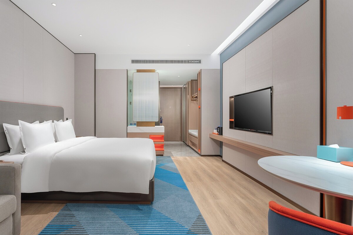 Quarto de hotel moderno com uma cama grande, televisão, secretária e banheiro.