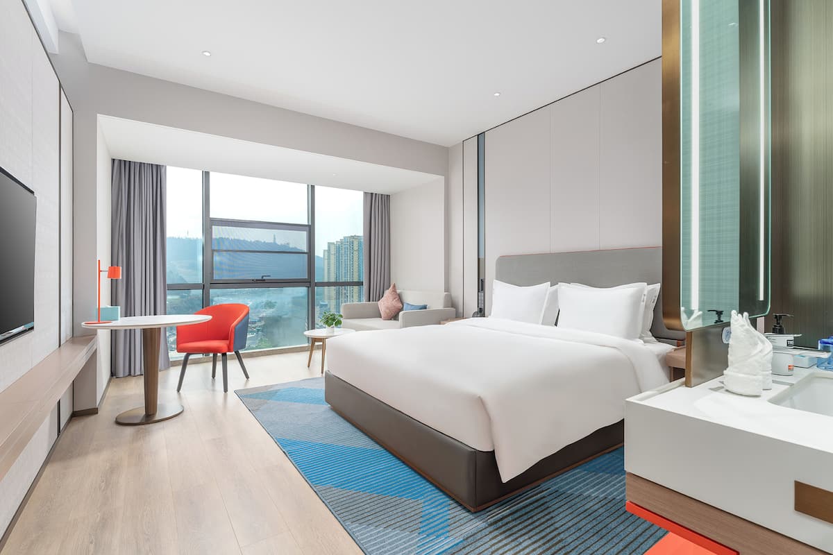 A modern hotel room with a large bed, a desk, a chair, and a TV.