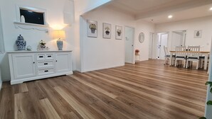 A spacious hallway with wooden flooring, white walls, and a dining area with white chairs and a table. - Unwind in Comfort, A Perfect Getaway Awaits Centrally Located Near All Amenities (Southport)