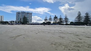 A beach with a large building in the background, palm trees, and a clear sky. - Unwind in Comfort, A Perfect Getaway Awaits Centrally Located Near All Amenities (Southport)