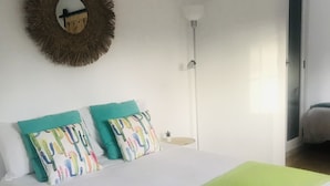 A bed with a green blanket, two pillows with a cactus pattern, a wall-mounted mirror, and a hanging light fixture.