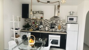 A compact kitchen with a glass dining table, white chairs, a washing machine, a microwave, and a stove.