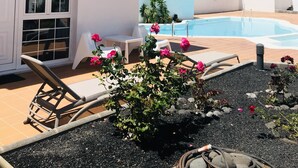 A white building with a pool, lounge chairs, and a garden with pink flowers.