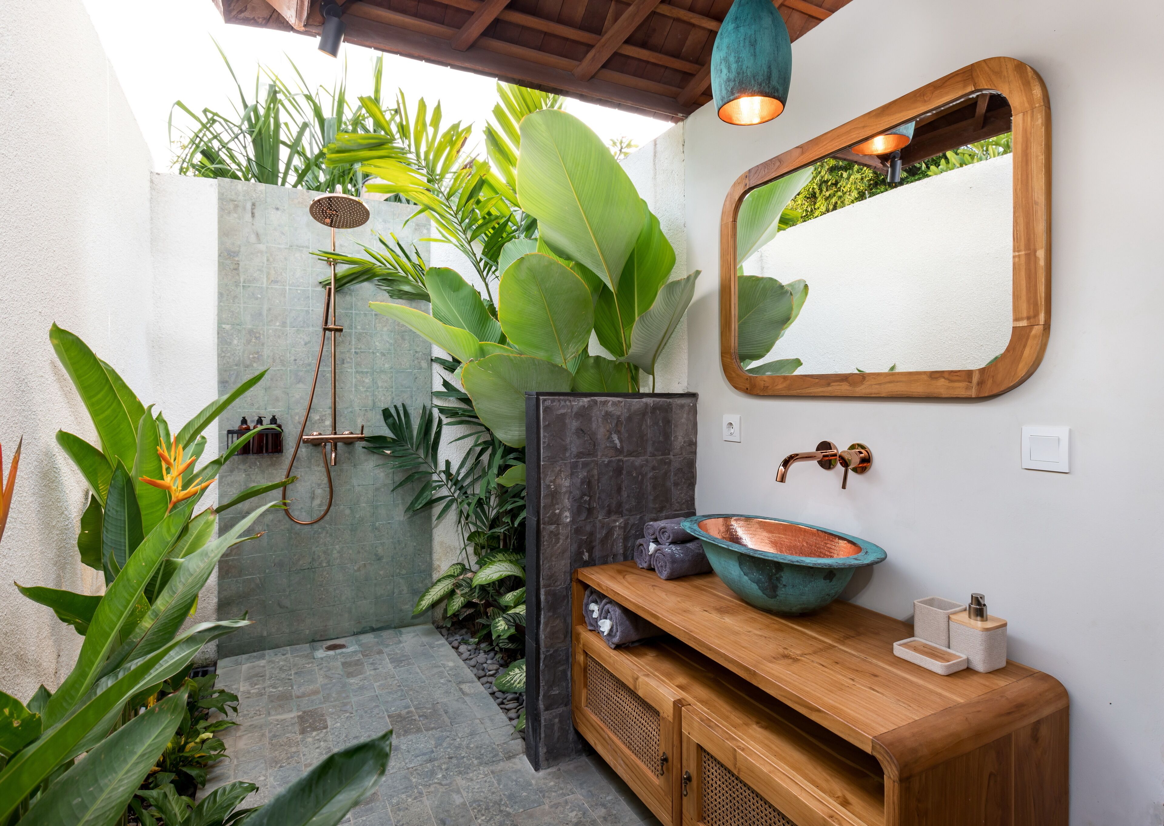 Een moderne badkamer met een douche, een houten wastafelmeubel, een grote spiegel en weelderige beplanting.