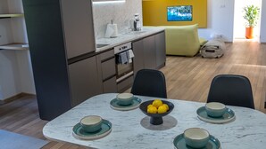 Eine moderne Küche mit dunklen Schränken, einer Marmorarbeitsplatte und einem Essbereich mit weißem Tisch und schwarzen Stühlen.