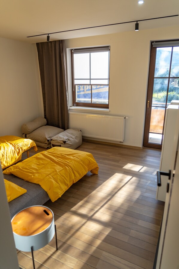 Un dormitorio con cama, ventana, radiador y puerta que da a un balcón.