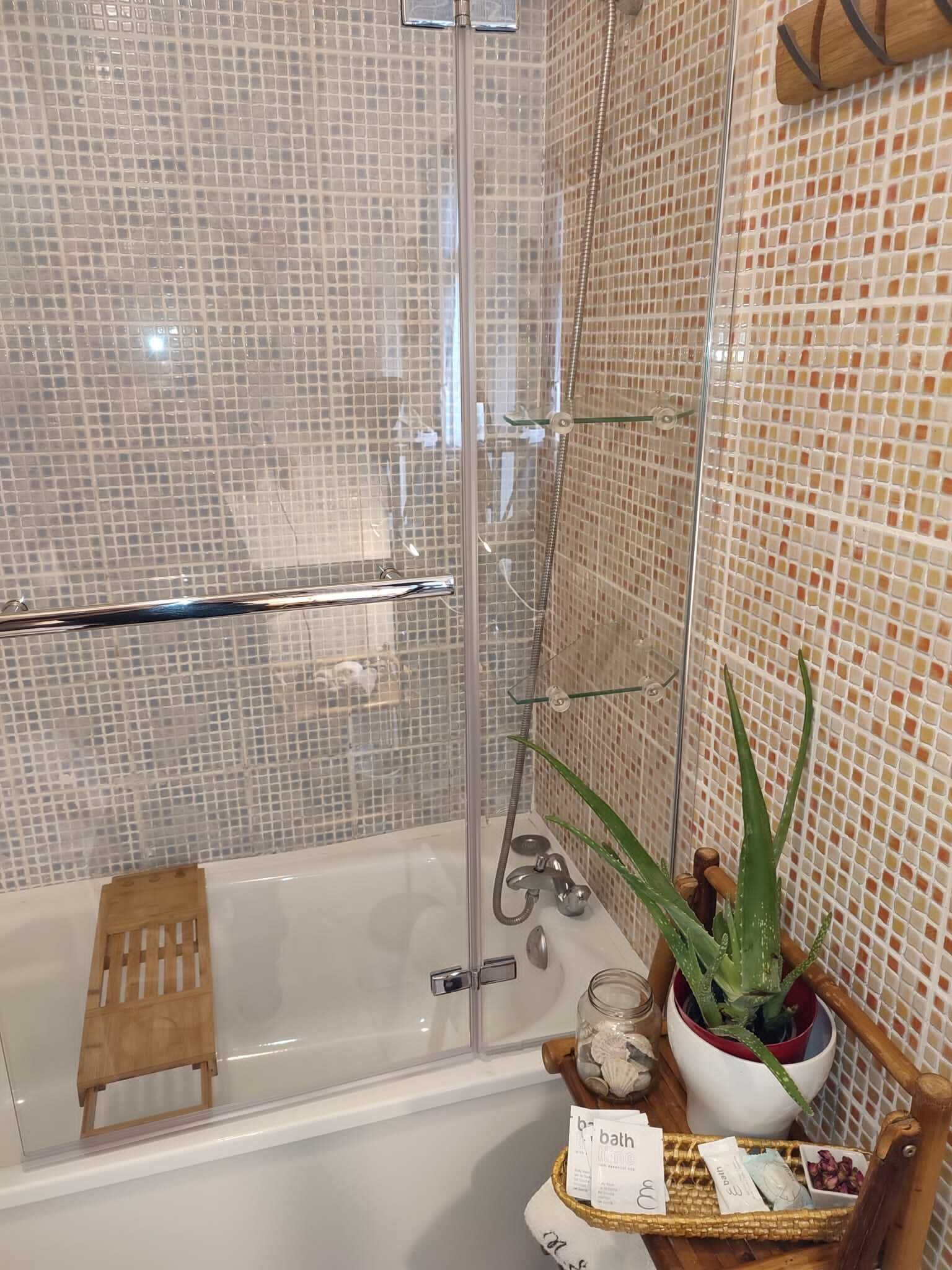 A modern bathroom with a glass-enclosed shower, a white bathtub, and a small wooden stool.