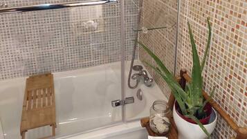 A modern bathroom with a glass-enclosed shower, a white bathtub, and a small wooden stool.