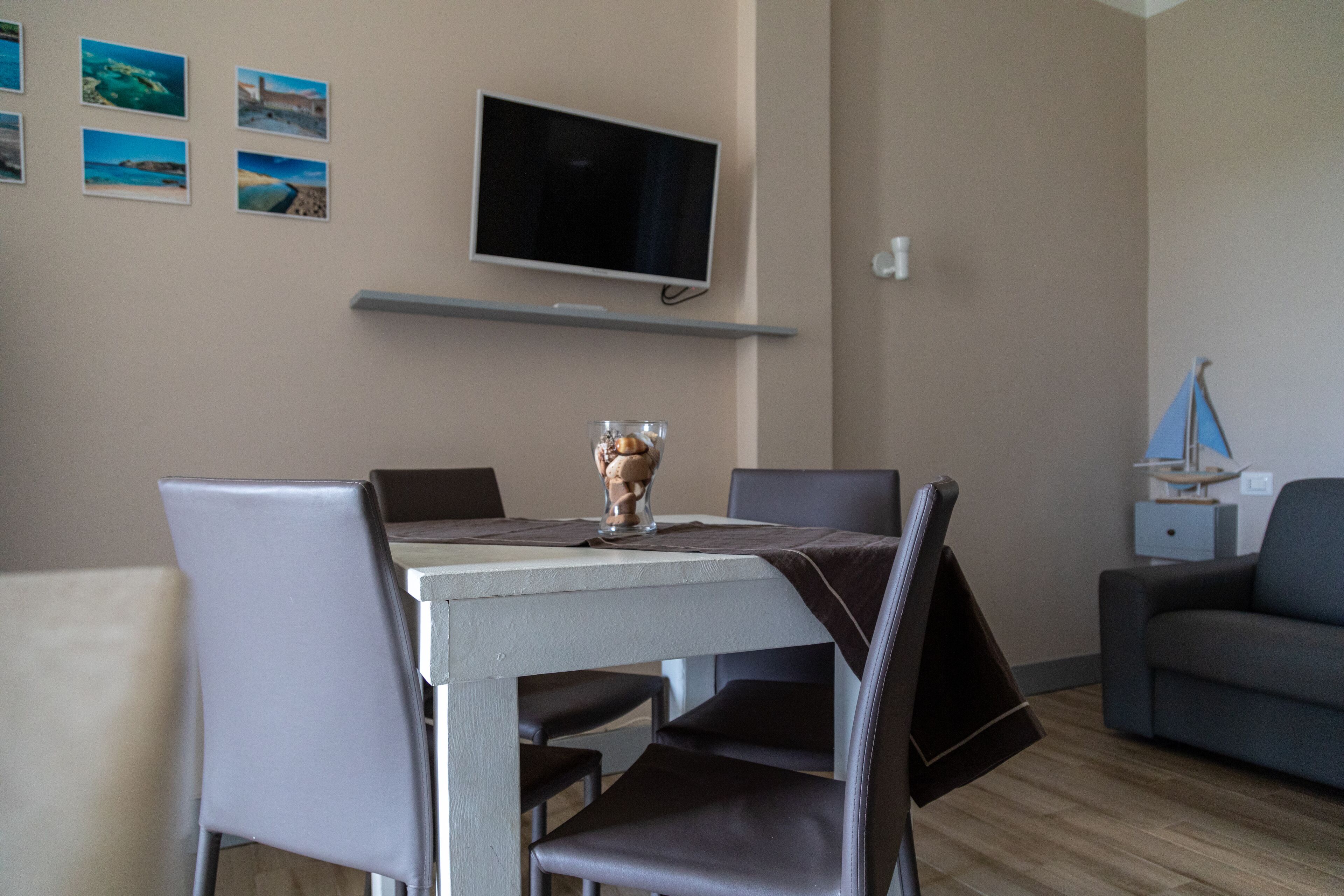 Uma sala de jantar com uma mesa, cadeiras, uma televisão presa à parede e uma pequena estante abaixo.