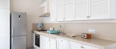 A modern kitchen with white cabinetry, a stainless steel refrigerator, a gas stove, and a small sink.