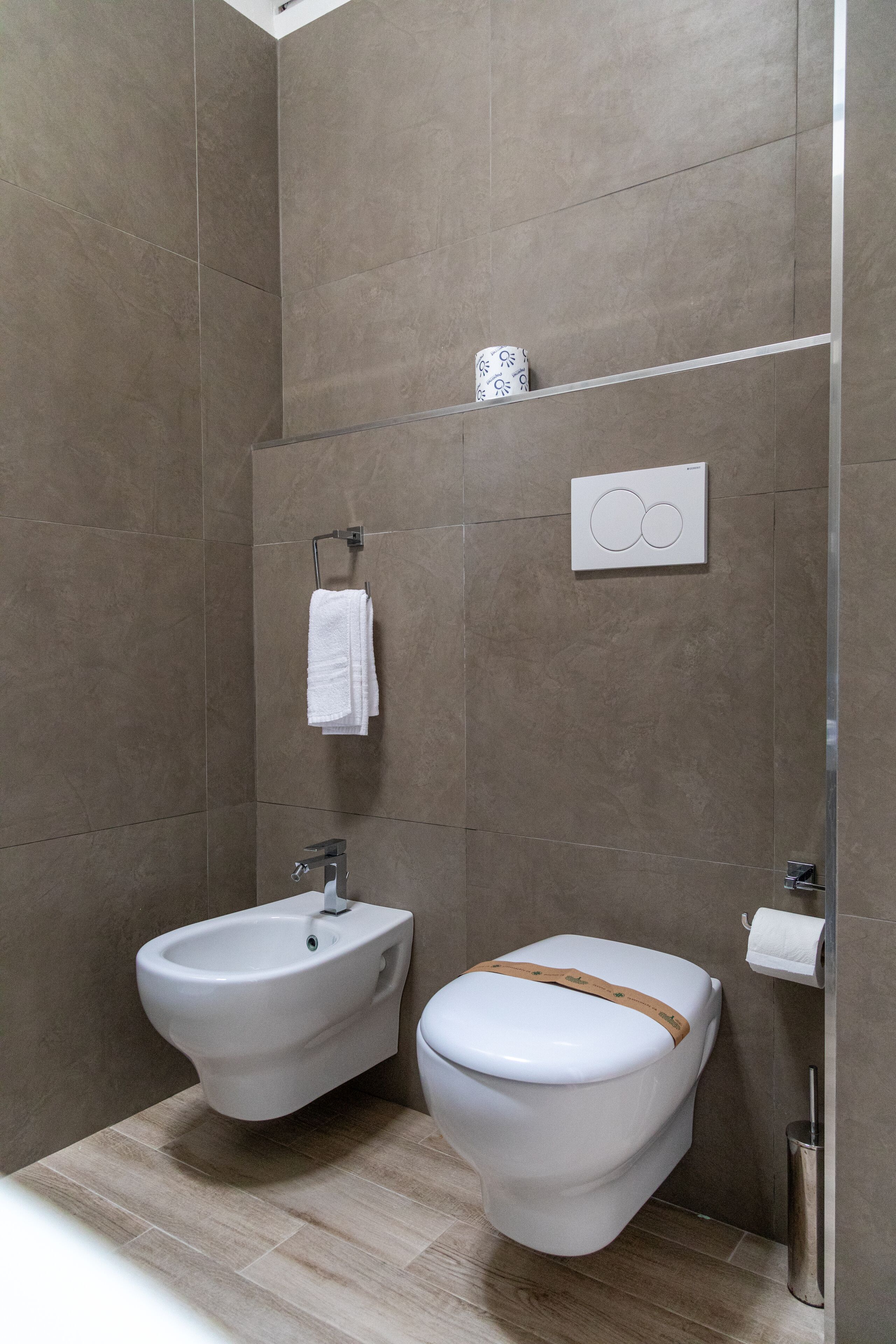 A modern bathroom with a bidet, toilet, towel rack, and a wall-mounted toilet paper holder.