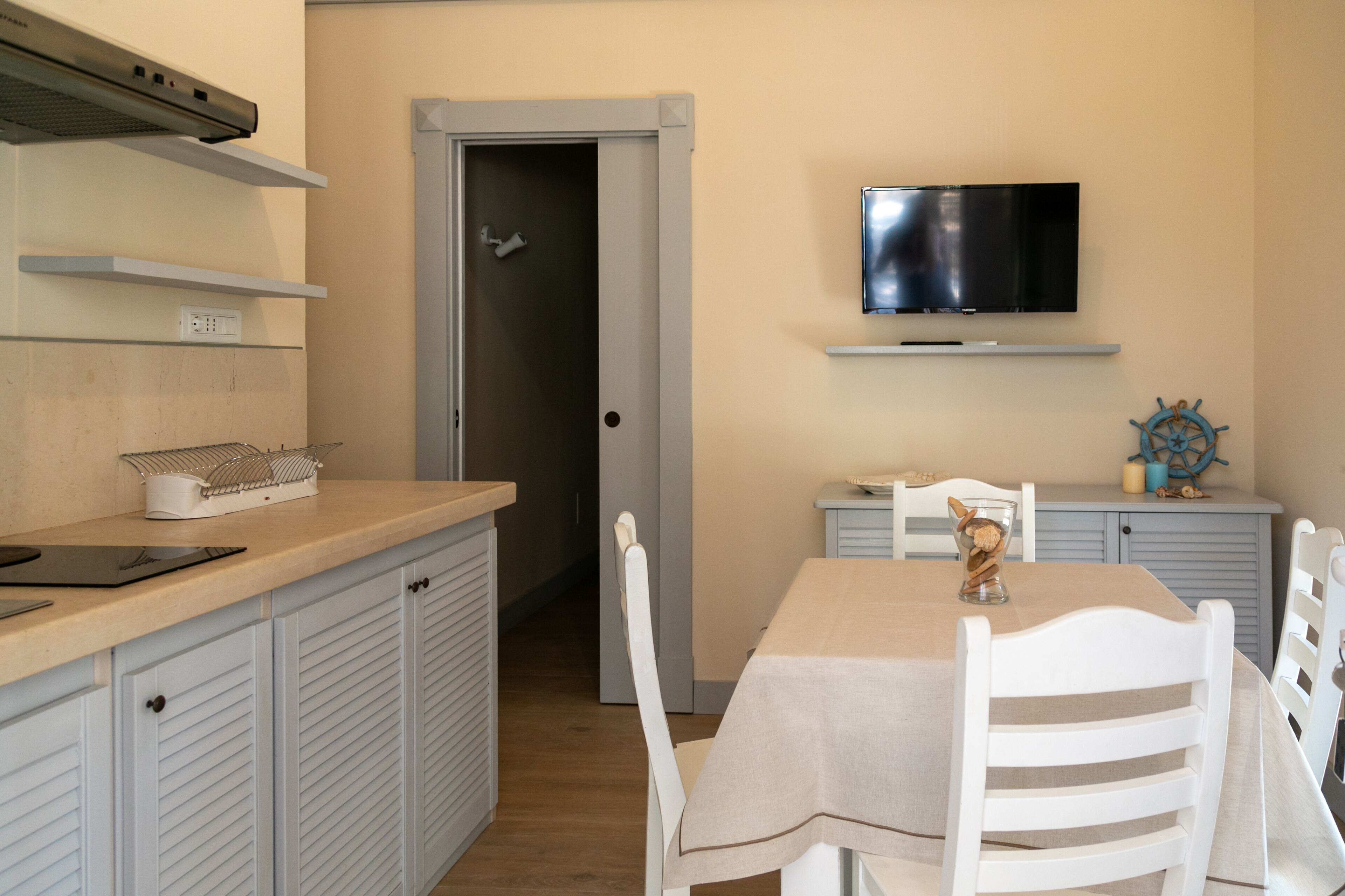 A compact kitchen with a dining area, a television mounted above the counter, and a door leading to another room.